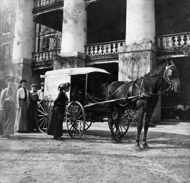 "View of Dughi's Ice Cream cart parked in from of the main building at Peace College with young women around the cart. Horse pulling cart is likely Nancy. Raleigh, NC, c.1900-1910's. From the Dughi Family Photo Collection, PhC.166, North Carolina State Archives, Raleigh, NC, call #: PhC_166_9. 