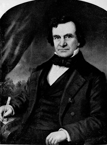 George W. Mordecai seated for a portrait. He is wearing a 3 piece suit, collared shirt, and bowtie. He has short, textured hair and is smirking. He is middle aged. 